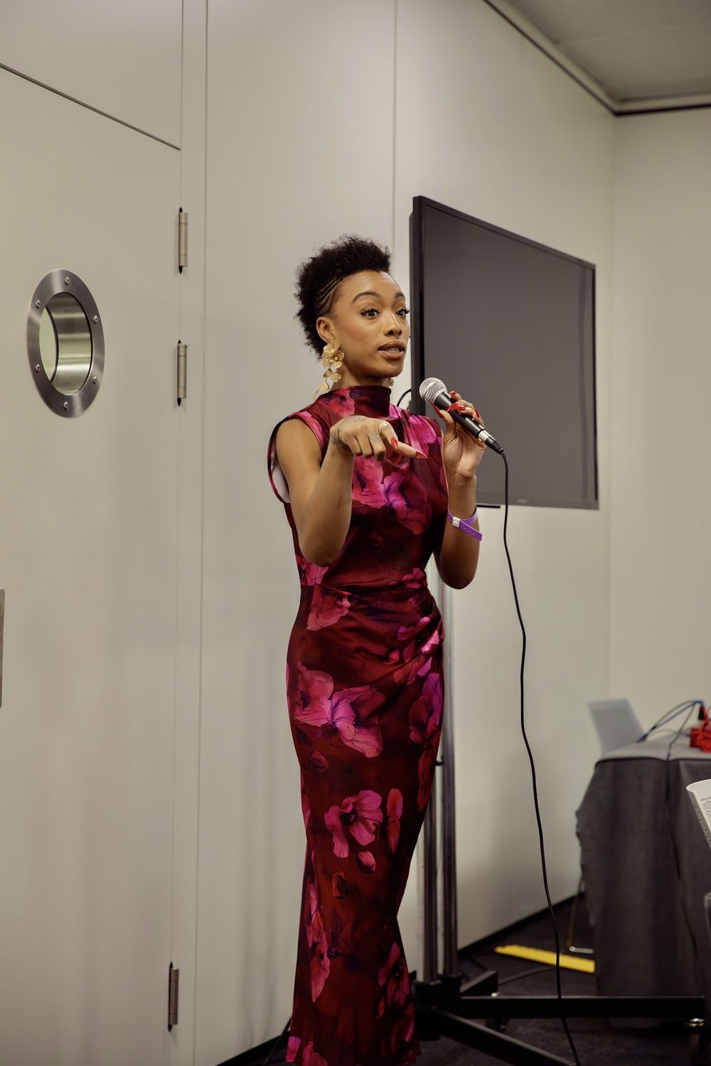 Paige speaking into a microphone in a raspberry dress