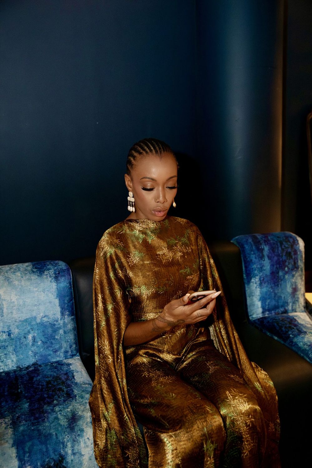 Paige in a gold outfit on a blue velvet sofa